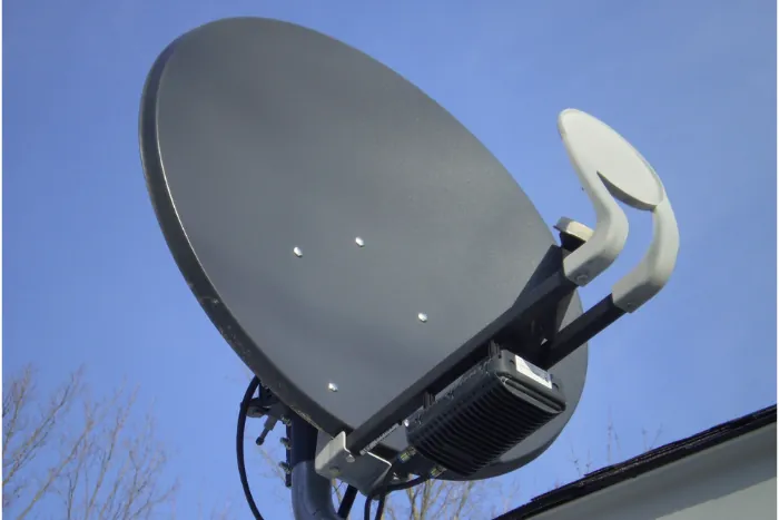 graue SAT-Schüssel auf einem Dach vor blauem Himmel